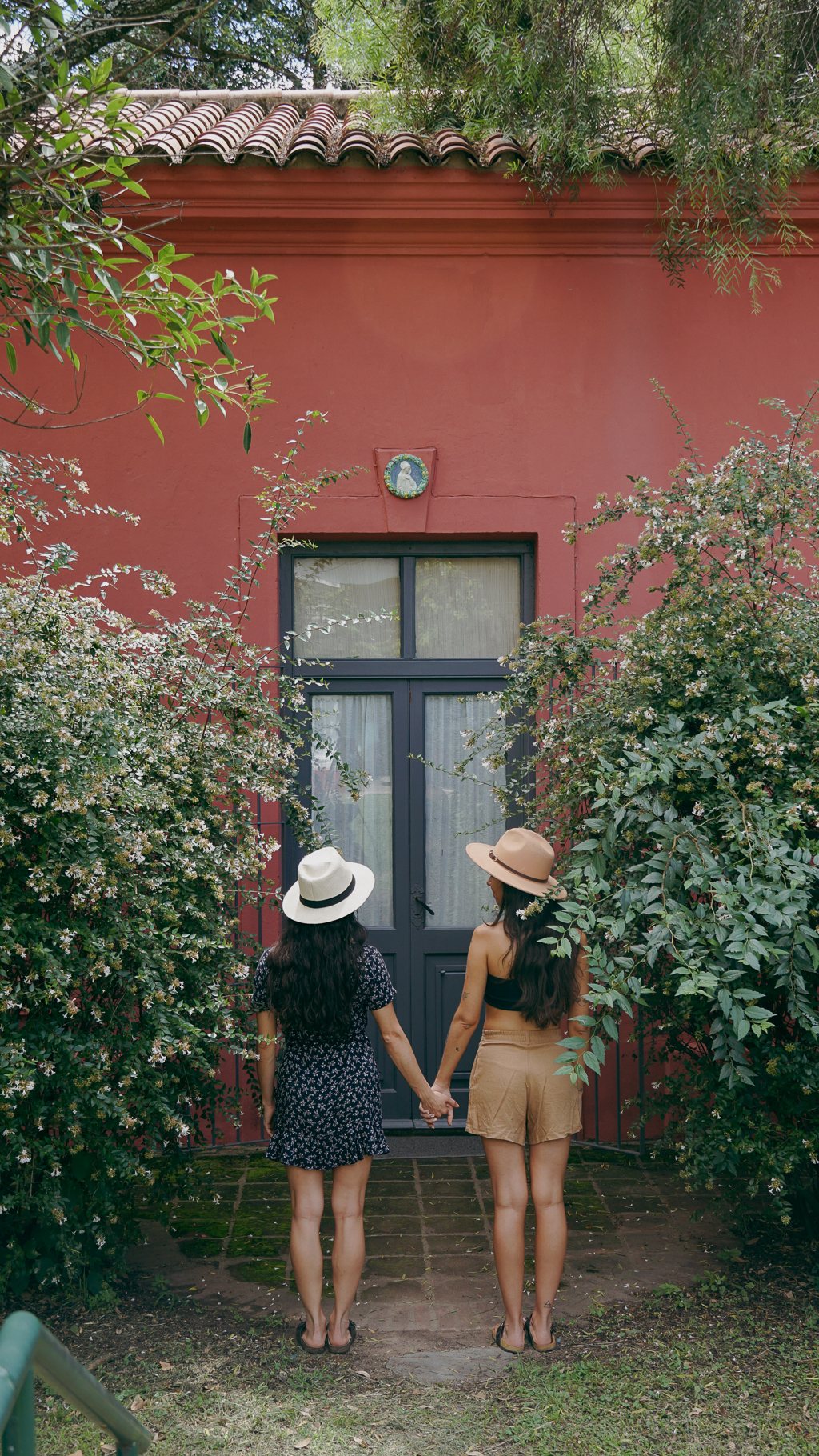 Pau y Juli de espaldas con sombreros frente a una casa rosa